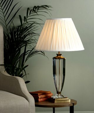 A laura Ashley glass based lamp with a white lampside on a small side table
