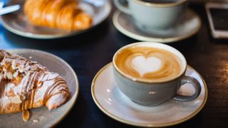 A coffee on a table with another coffee and two croissants