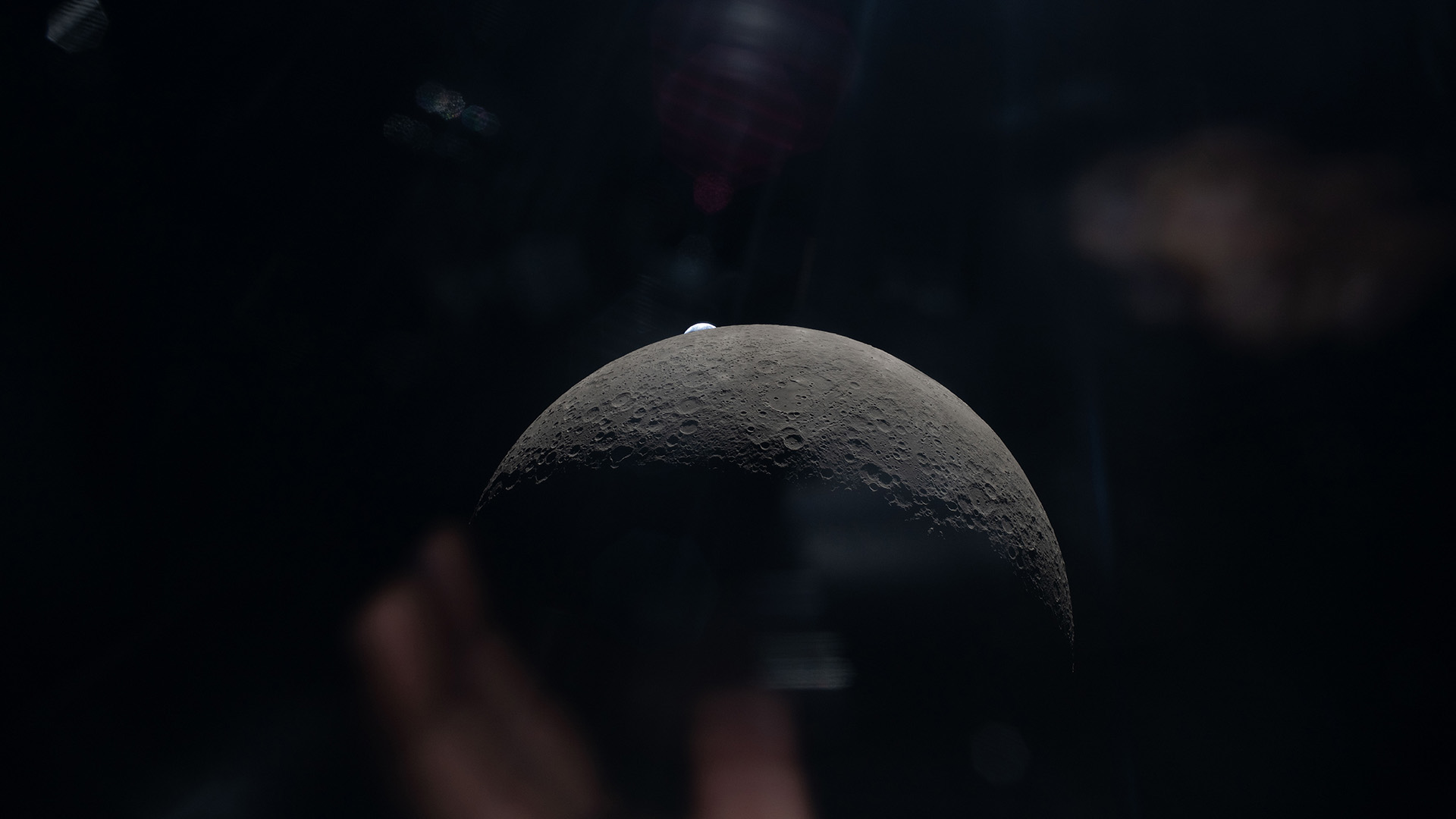 A view of the gray sphere of the moon in space, with a faint blue Earth behind it.