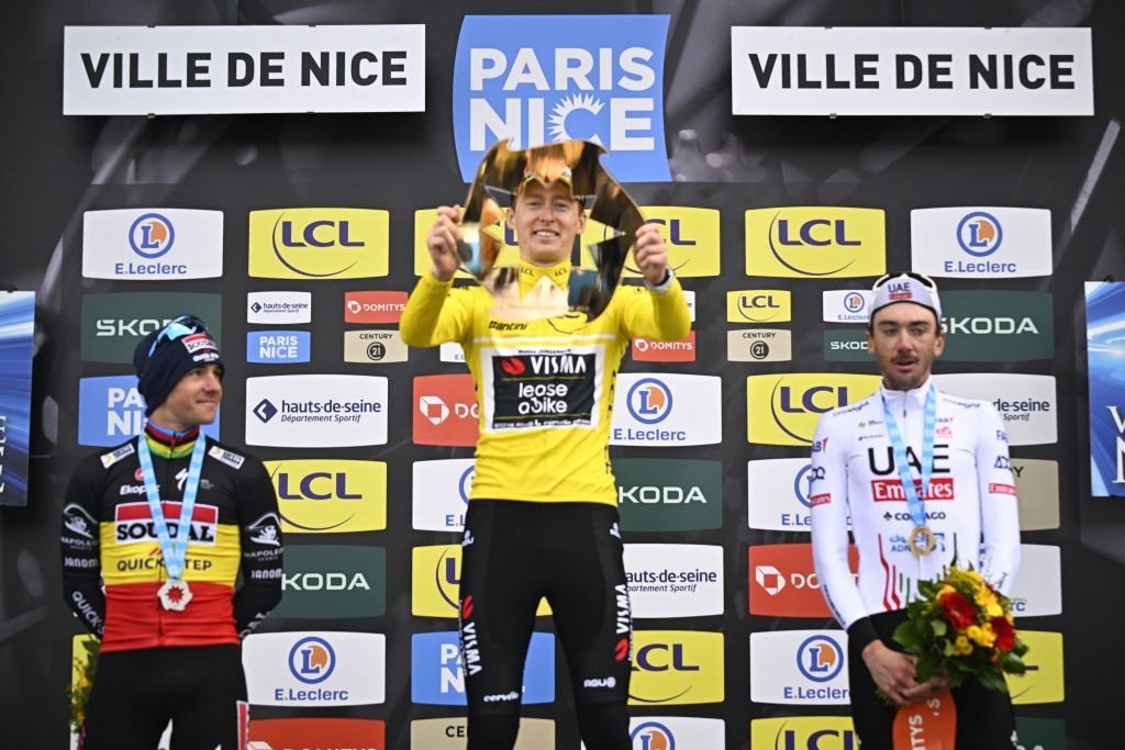 Matteo Jorgenson holds up the trophy on the final podium of Paris-Nice in 2024 flanked by second place Remco Evenepoel and third placed Brandon McNulty