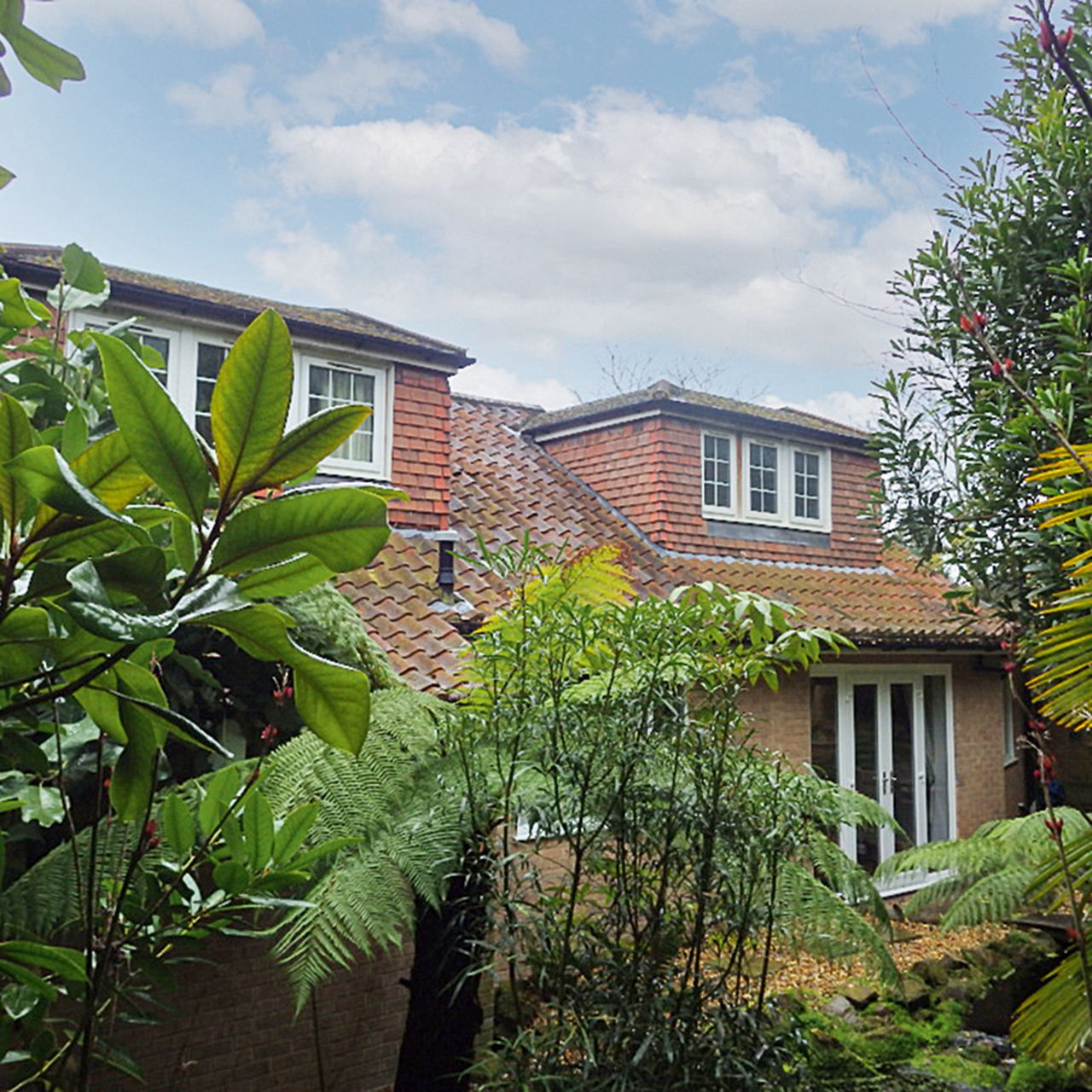 Exterior of the back of a 1970s brick house surrounded by lush trees