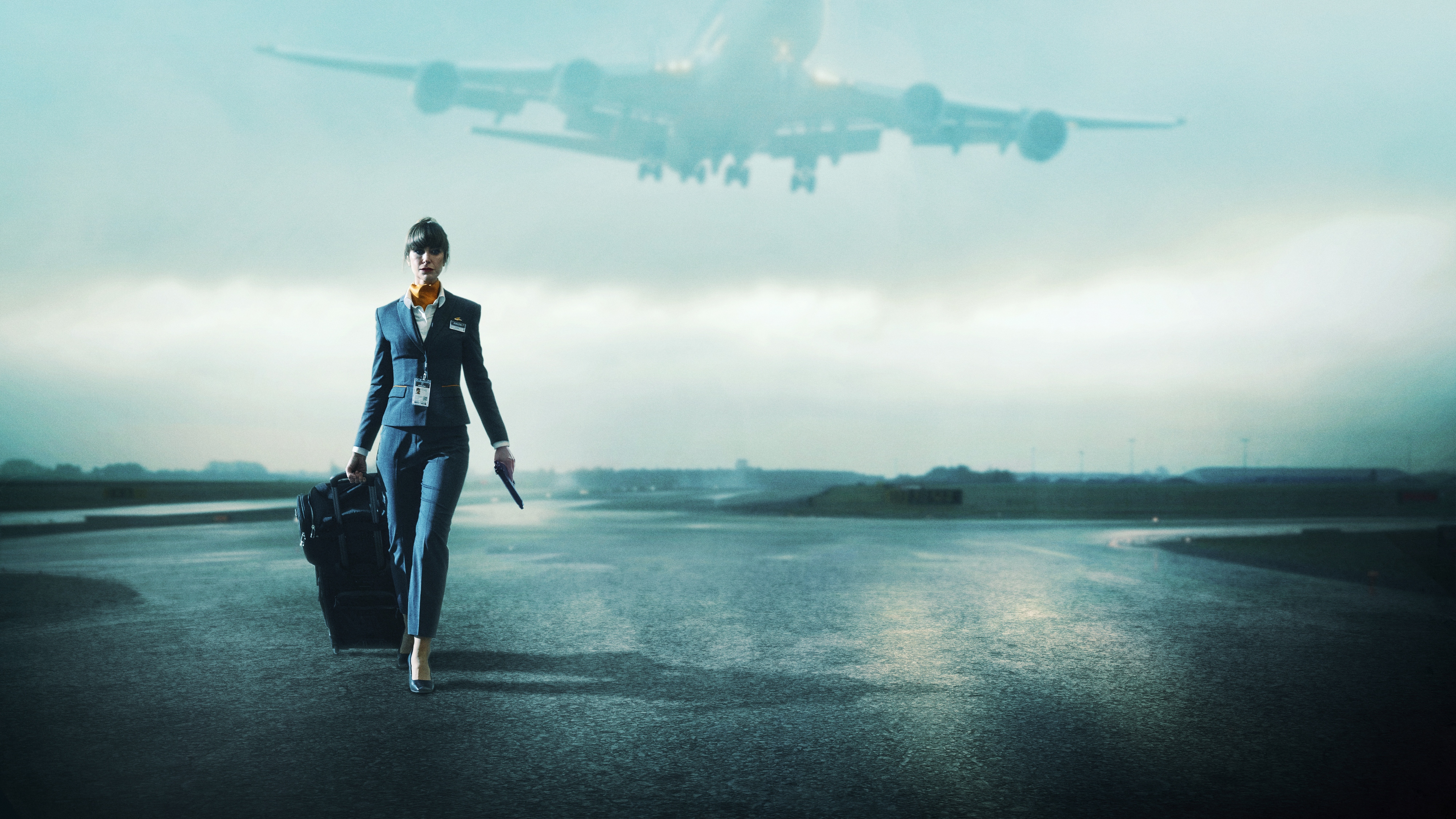 Katherine Kelly as Jo walking along an airport runway in her flight attendant uniform while a plane takes off overhead 