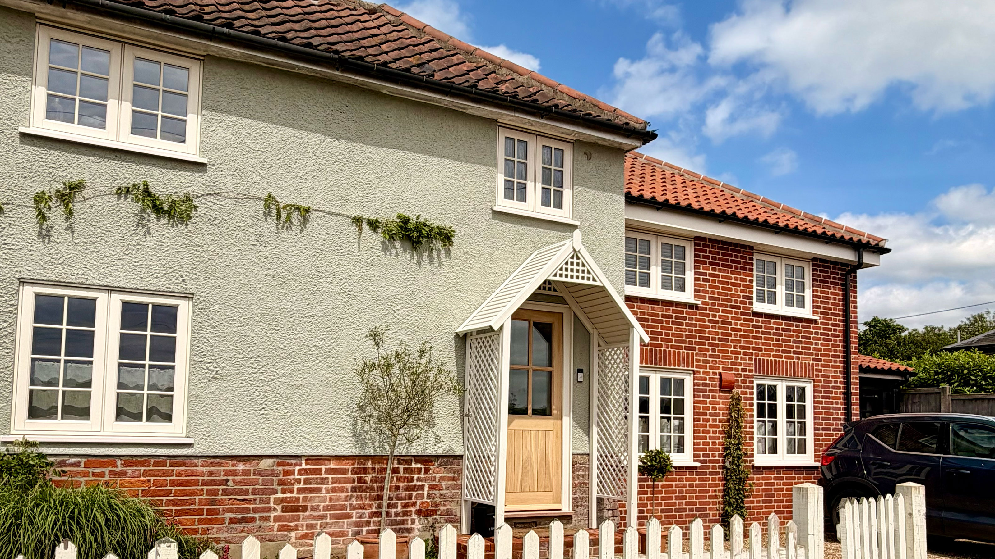 Pale green home with brick base, with cream porch and matching wooden fence