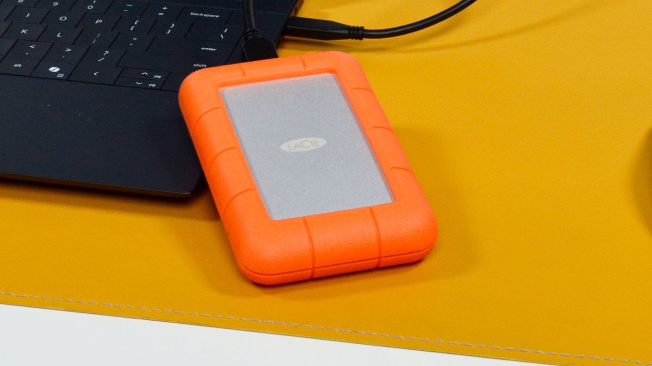 A LaCie Rugged Mini external hard drive on a desk with a laptop