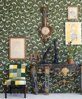Green and white patterned wallpaper in entryway, wooden console table, checkered chair, artwork and clock on walls