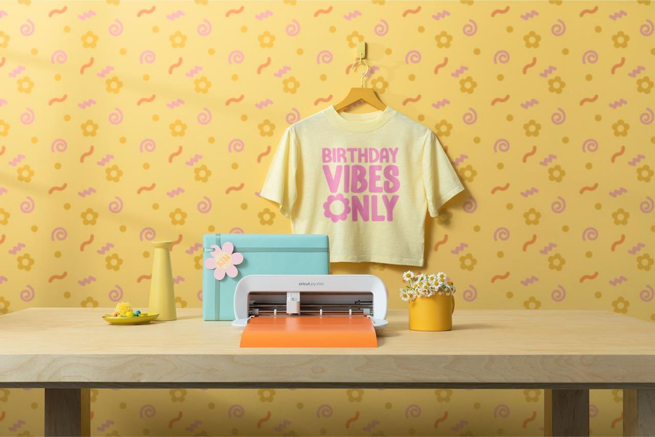 The Cricut Joy Xtra cutting machine on a crafter&#039;s desk and a bright yellow wall