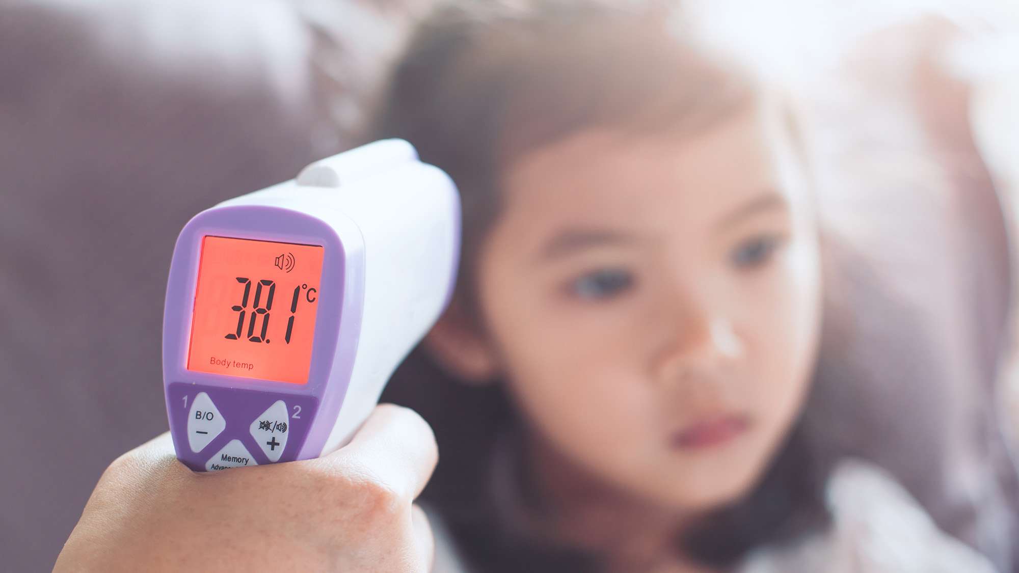 Mother measures her young daughter's temperature with a forehead thermometer