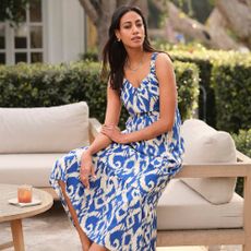 Woman sat on a yard chair in a blue patterned Evereve dress