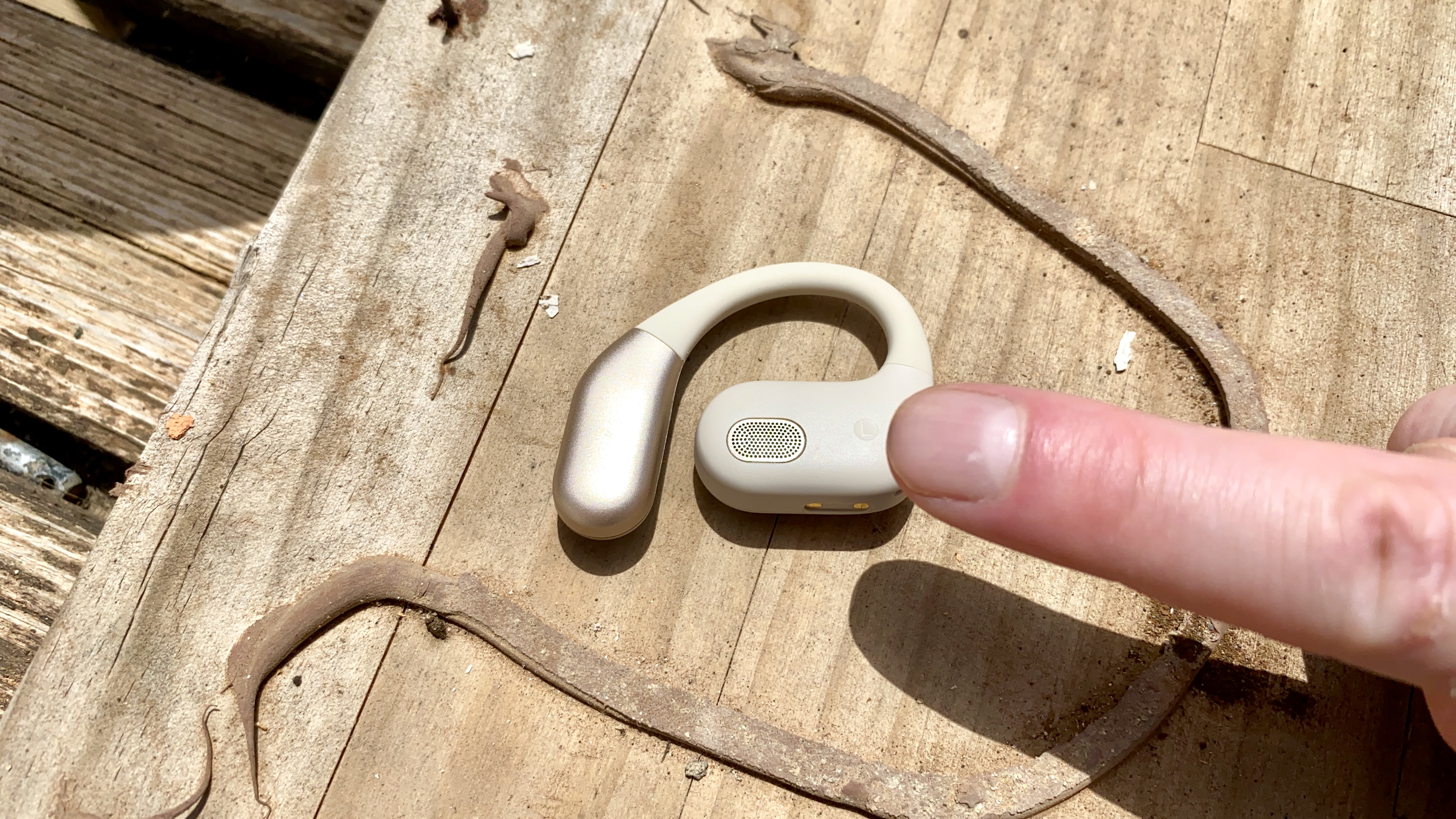 Panasonic RB-F10 open earbuds, with a finger in shot to provide a sense of scale, on a wooden surface