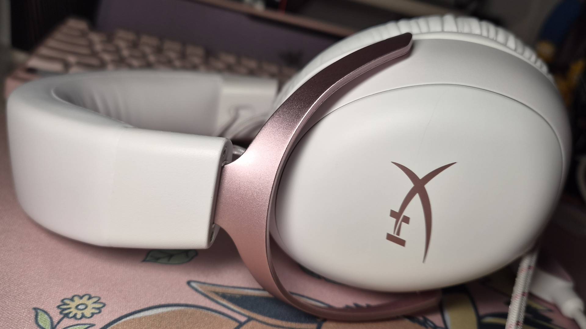 Photo of the White-Pink HyperX Cloud III wired gaming headset laying on a pink mousepad.