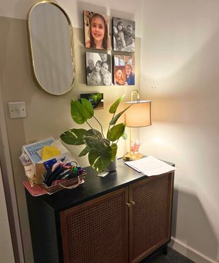 My black and wicker sideboard with plant and pile of paperwork on the right