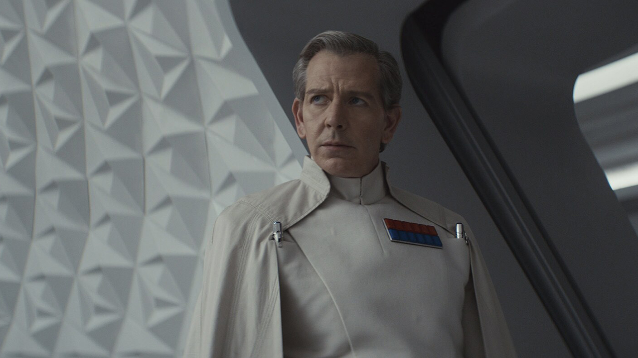 Still from the Star Wars TV show Andor. Ben Mendelsohn returns as Orson Krennic. He is wearing a white uniform and cape, with a lot of red and blue badges on his chest.