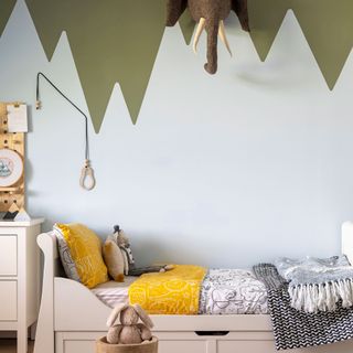 Kid's bed in front of a wall with a mountain scape painted mural in green and blue