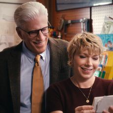 A father (Ted Danson as Charles) looks over the shoulder of his adult daughter (Mary Elizabeth Ellis as Emily) as she holds a set of photos, while the pair stand in a garage full of engineering tools, in episode 108 of A Man on the Inside.