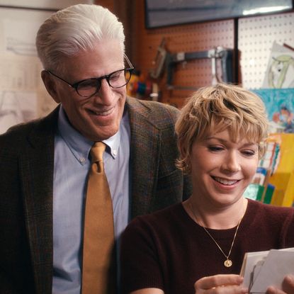 A father (Ted Danson as Charles) looks over the shoulder of his adult daughter (Mary Elizabeth Ellis as Emily) as she holds a set of photos, while the pair stand in a garage full of engineering tools, in episode 108 of A Man on the Inside.