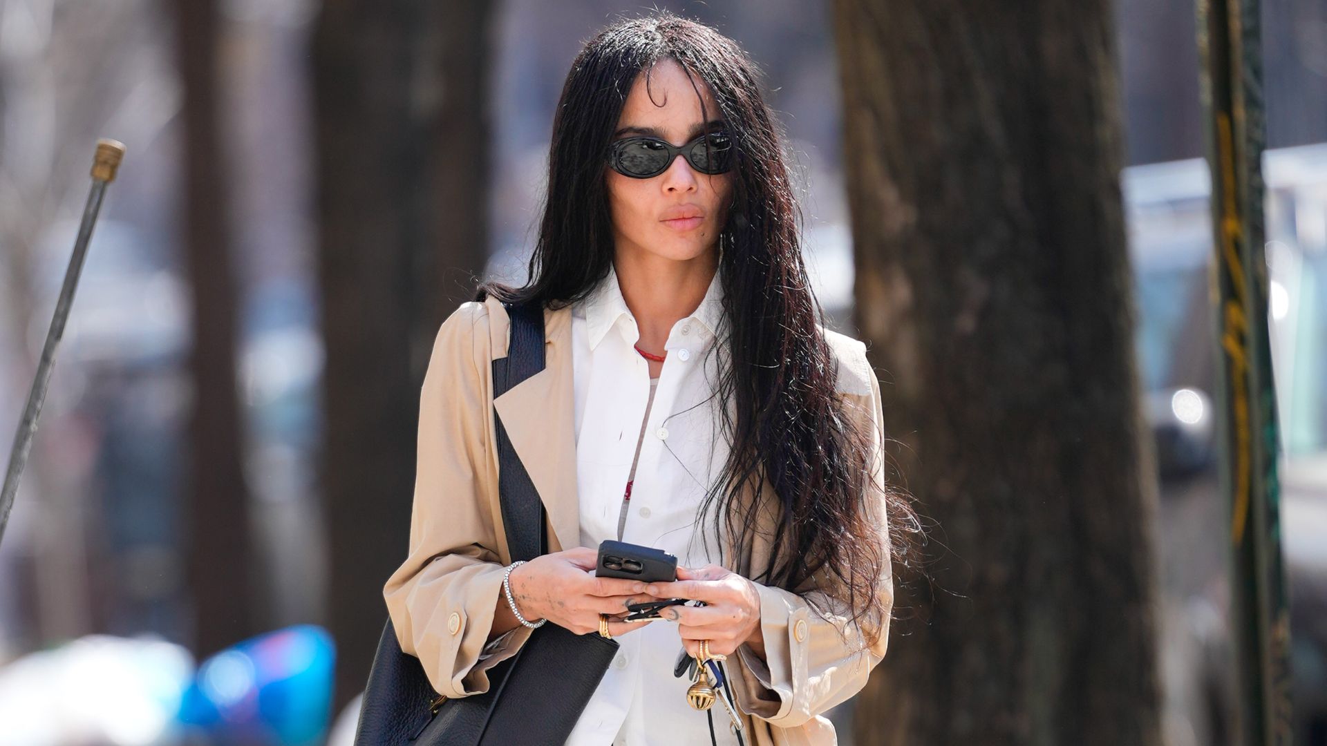 Zoe Kravitz walks down the streets in New York wearing a white shirt with bootcut trousers, square-toe boots and a beige trench coat.