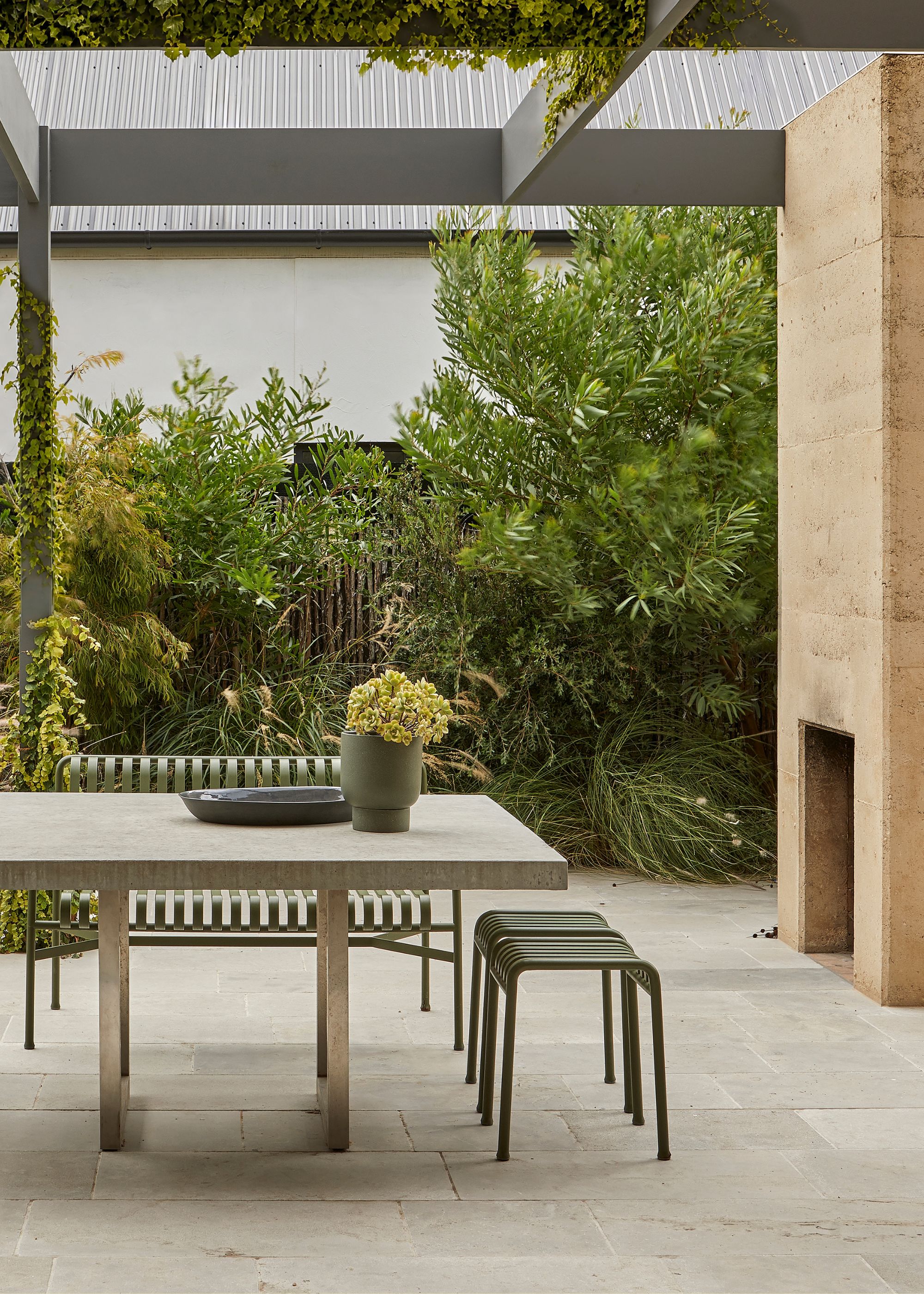 An outdoor dining room with a green metal seat set and a stone dining table, and a fireplace