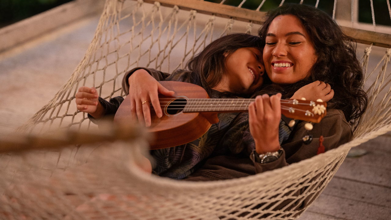 Maia Kealoha and Sydney Agudong lay together in a hammock smiling in Lilo and Stitch.