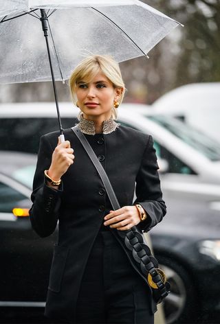 a close street-style photo of a woman wearing a vintage Chloe bag with a black jacket, black pants, gold earrings, and a clear umbrella