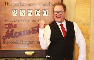 Alan Carr poses in front of a board for The Mousetrap.