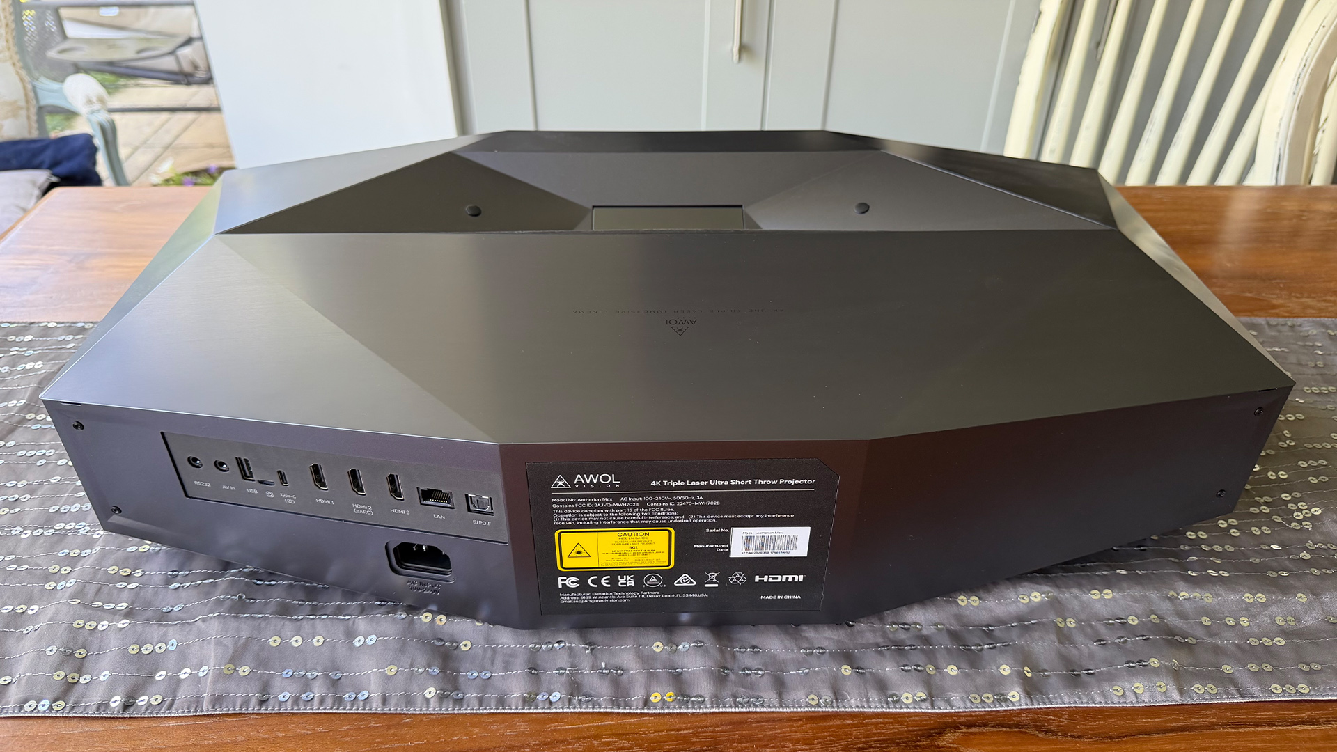 AWOL Vision Aetherion Max ultra short throw projector on grey table runner on dining table, rear of device showing connetions