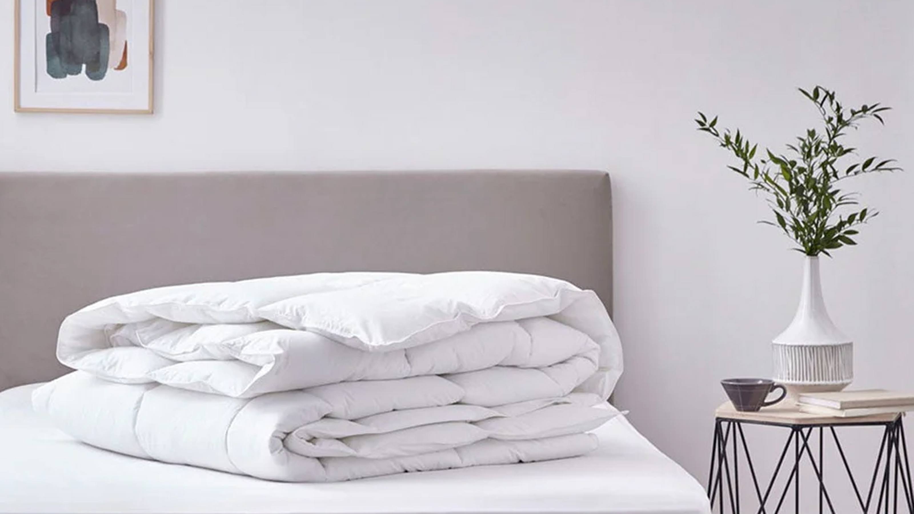 A folded duvet on a stripped bed with a side table