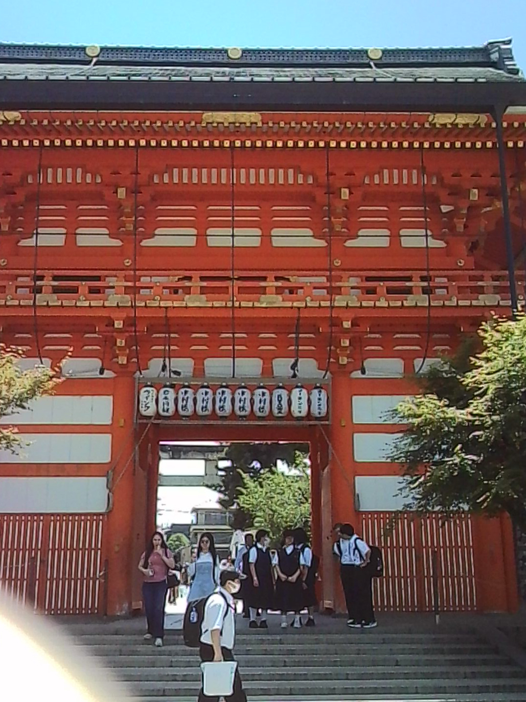 Red Japanese shrine gate with lanterns and visitors gathered beneath it.