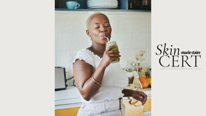 A young Black woman with glowing skin drinking a green smoothie in her kitchen