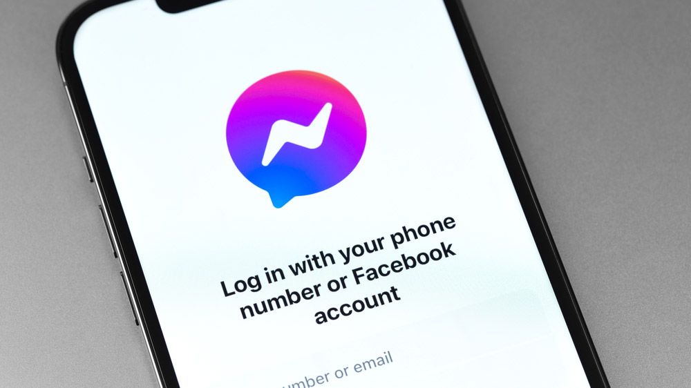 The Facebook Messenger logo on an iPhone screen along with the text &#039;Log in with your phone number or Facebook account.&#039;