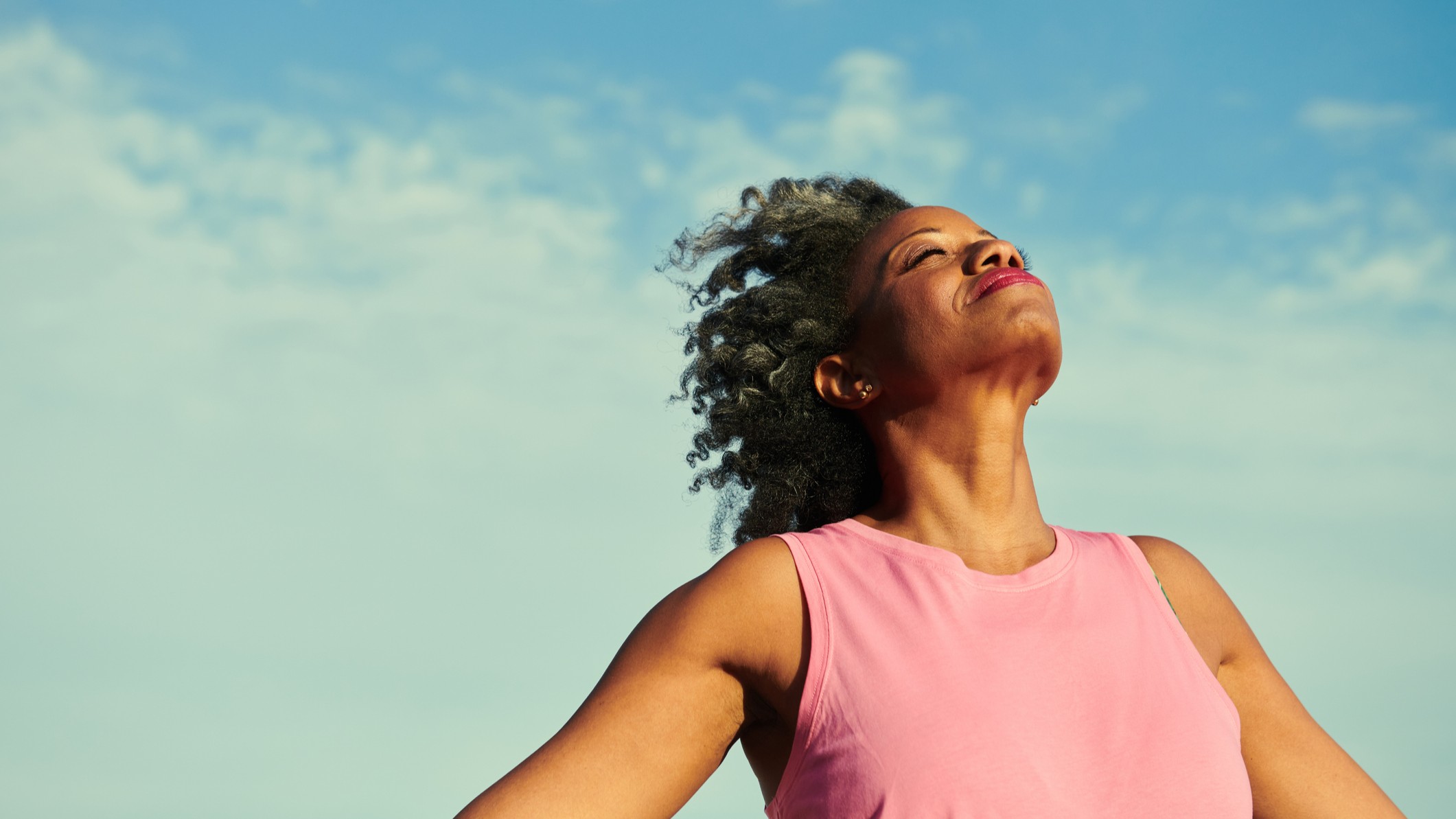 A woman in her fifties turns her face to the sky, with eyes closed. She looks very happy.