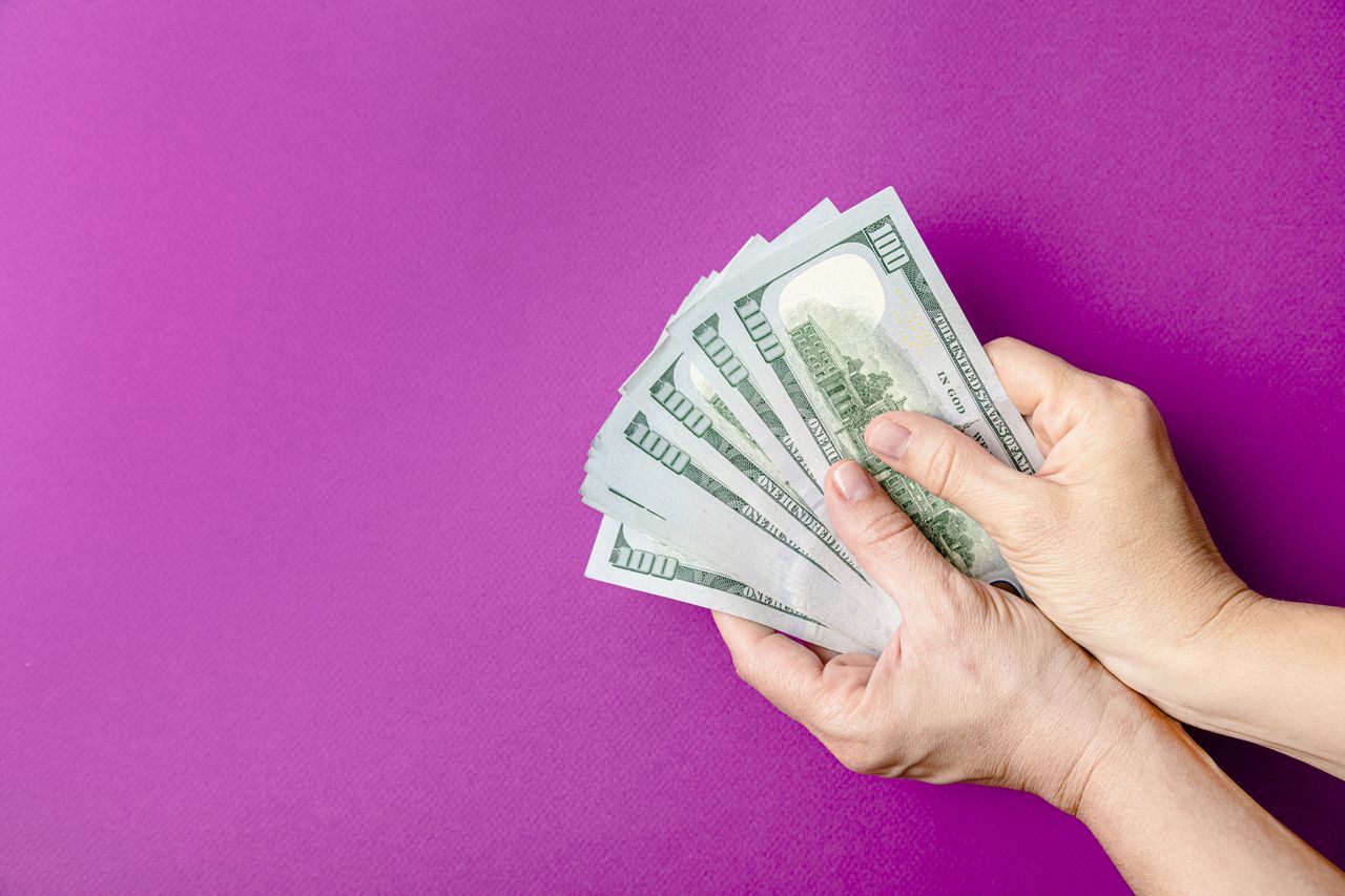 Image of person&#039;s hands holding a fanned out stack of cash.