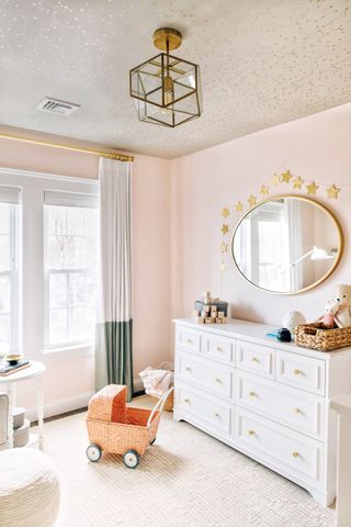 Starry ceiling in pink colored kids bedroom with white modern furniture and gold accessories