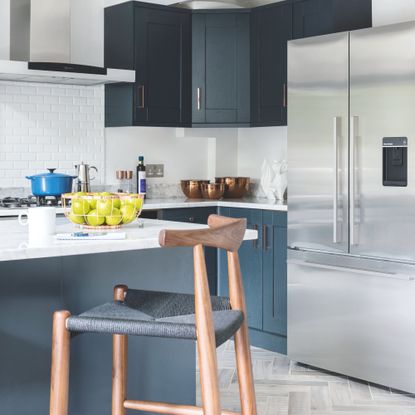 Large fridge freezer in a kitchen with white marble counter tops and blue cabinets