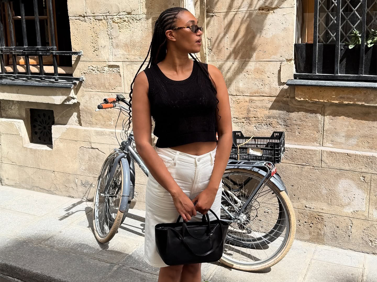 A woman wearing a pair of white jean shorts, a knit black top, and a black bag.