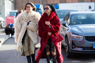 Two women at Copenhagen Fashion Week walk through a parking lot wearing faux fur coats