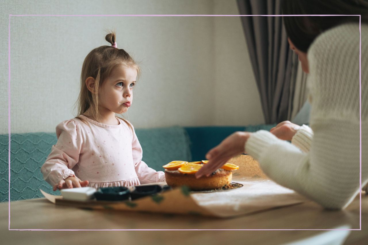 A young girl frowning at her mother over a kitchen table