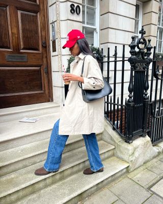 Georgia wears a red hat, trench coat, black handbag, wide-leg jeans, and brown suede boots.