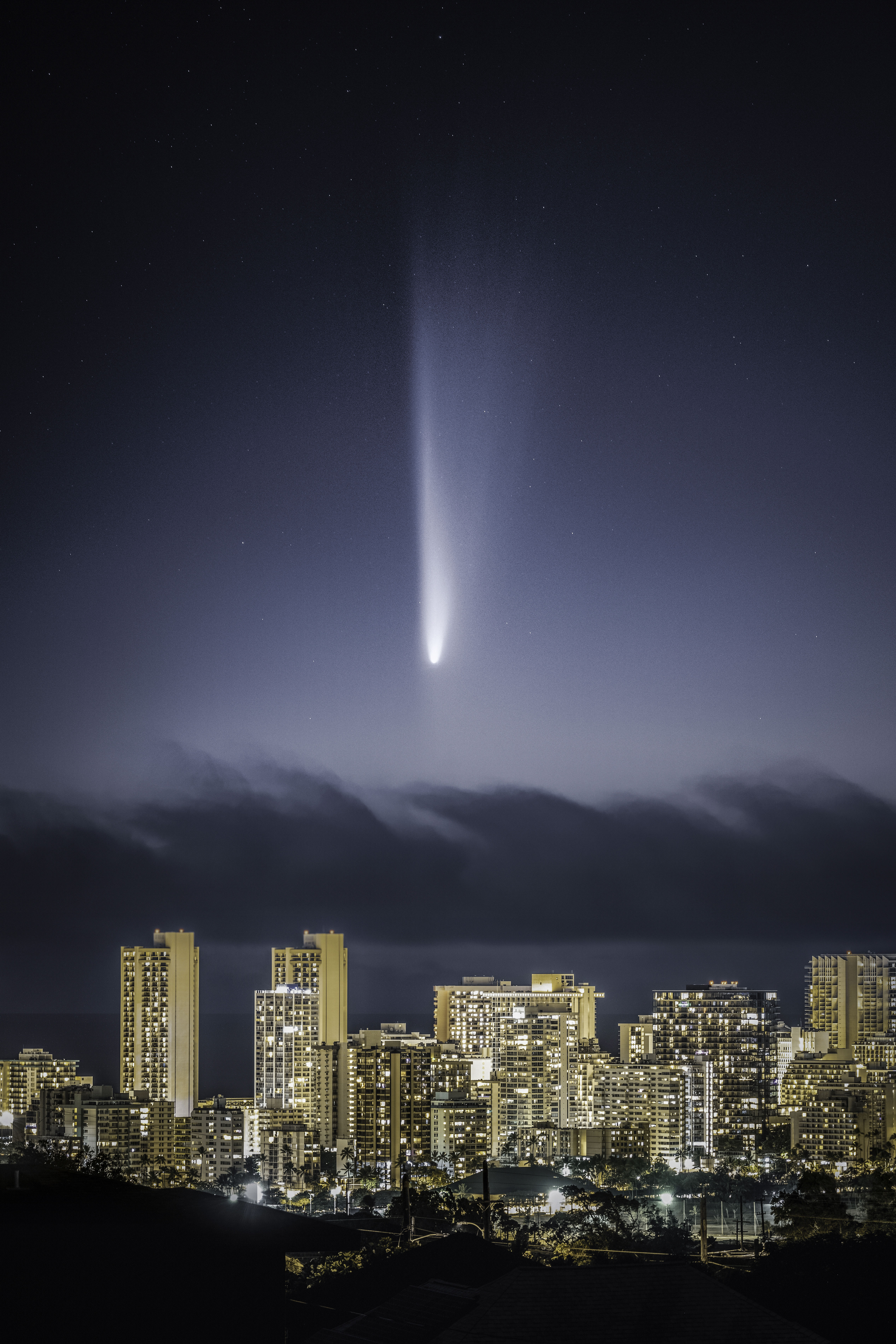 A large comet streaks over the bright city of Waikiki with large golden skyscrapers