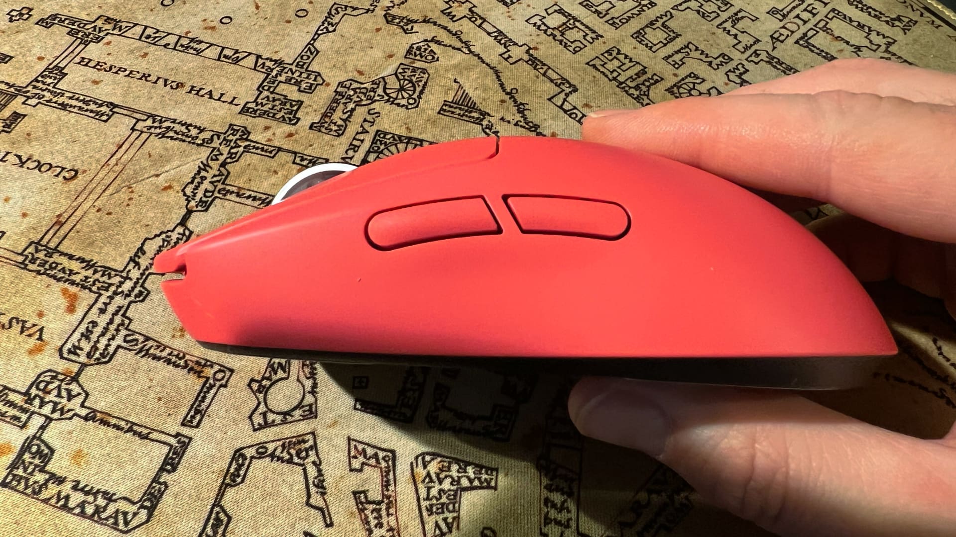 En hand håller upp en rosa Logitech G Pro X Superlight 2 och visar knapparna på sidan.