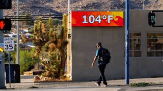 A man walks on the sidewalk in front of a temperature monitor that reads 104 F in Joshua Tree, California.