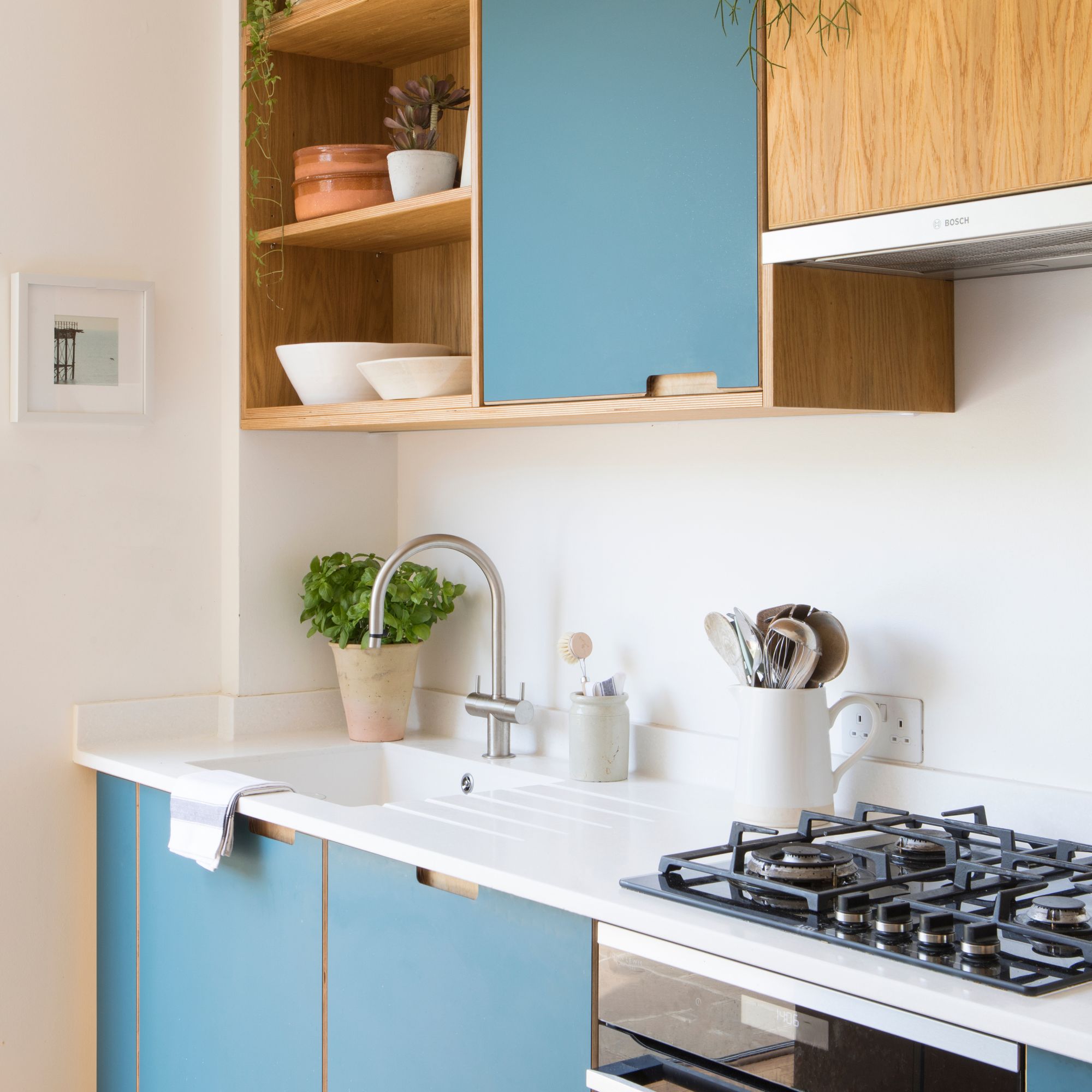 White painted kitchen with a white worktop and splashback, and blue cabinets with a sink