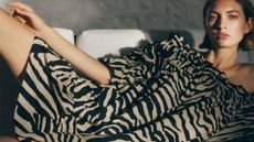 A female model laying on her side wearing a brown and black tiger print dress from H&M.