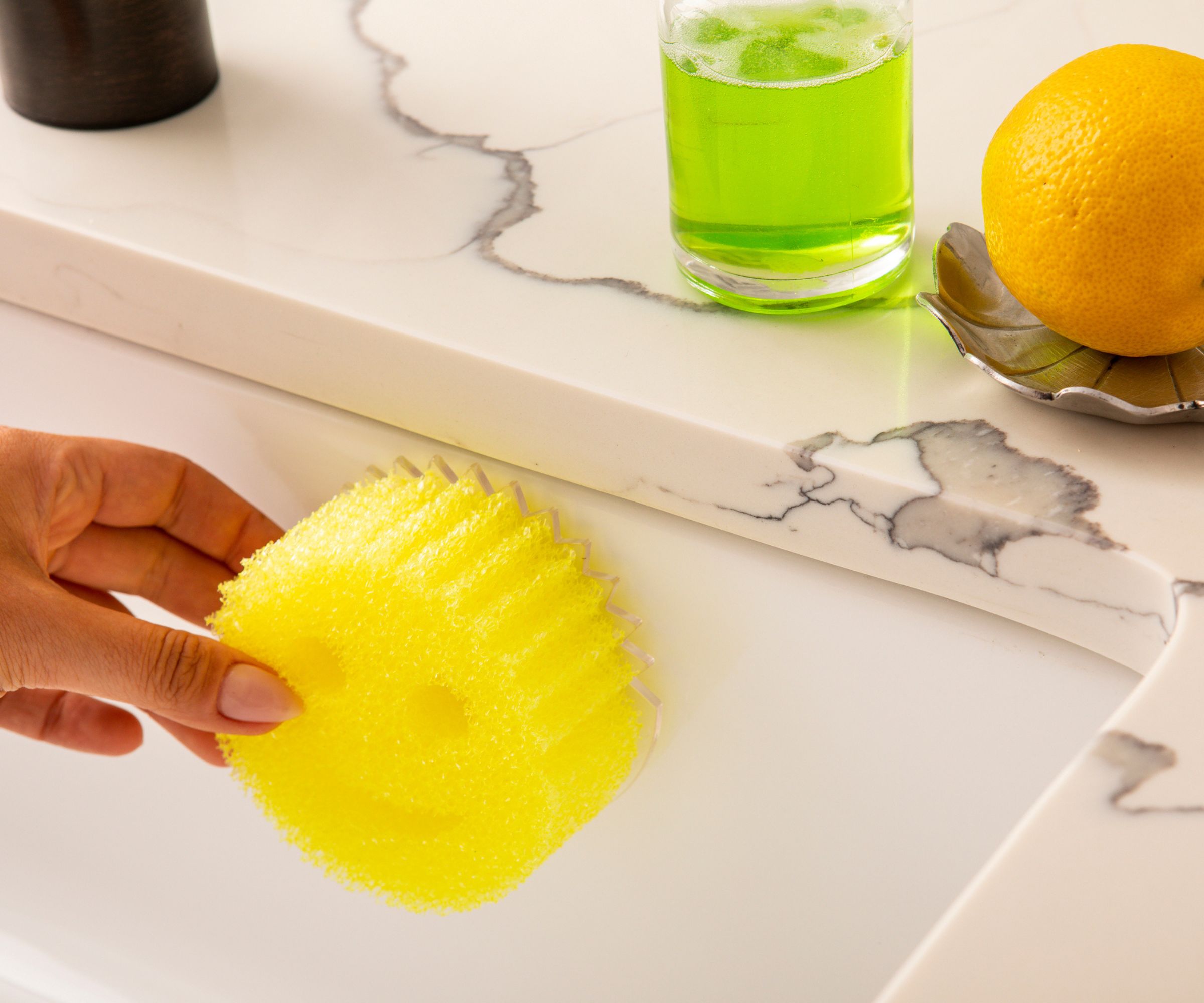 Someone putting a yellow scrub daddy sponge on a scrub daddy caddy in a white sink.