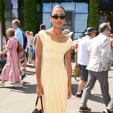 Olivia Dean wears a butter yellow dress and cream heels with a brown suede bag to Wimbledon.