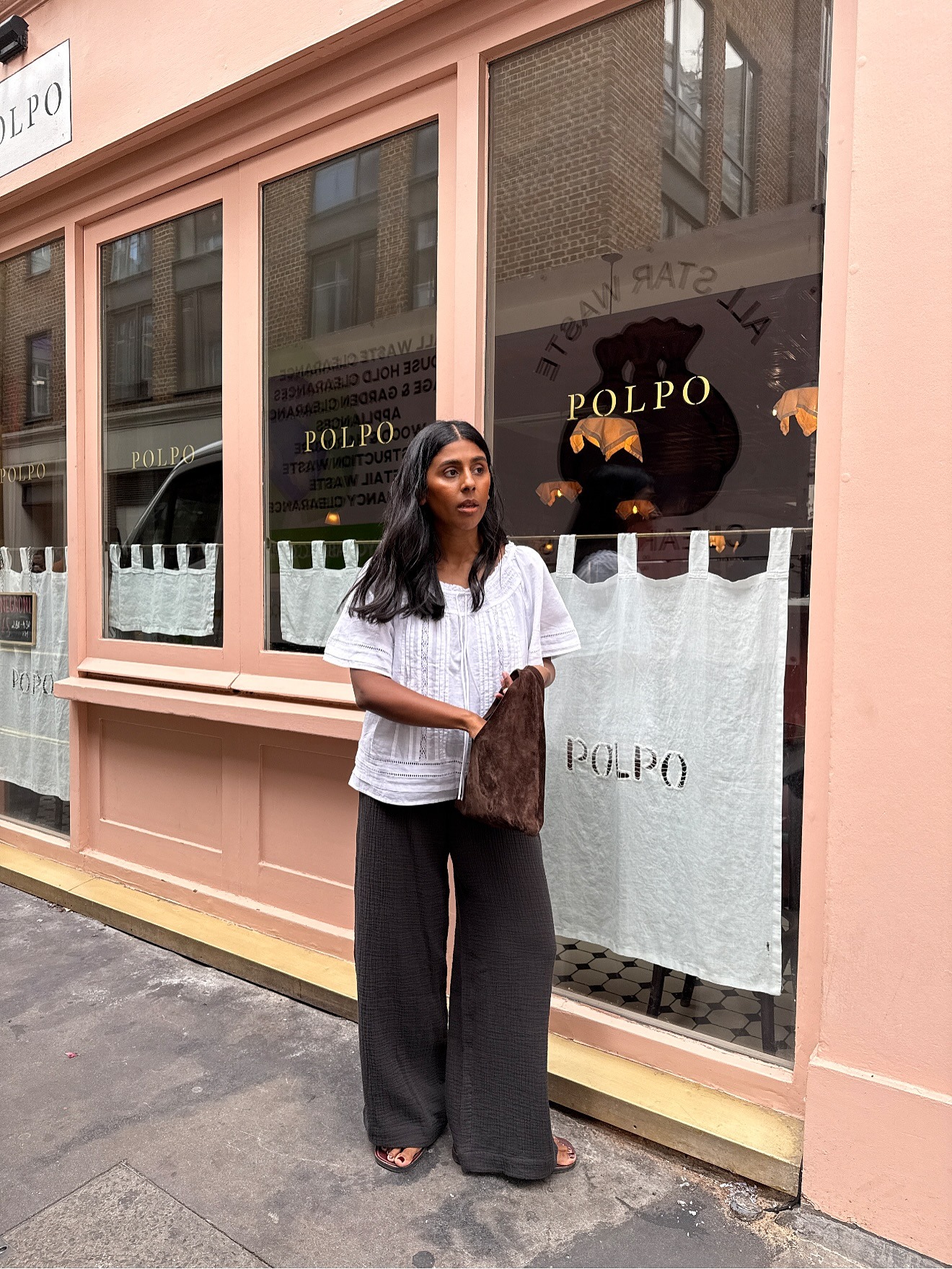 European influencer wearing a white summery top, brown pants, and flip-flops