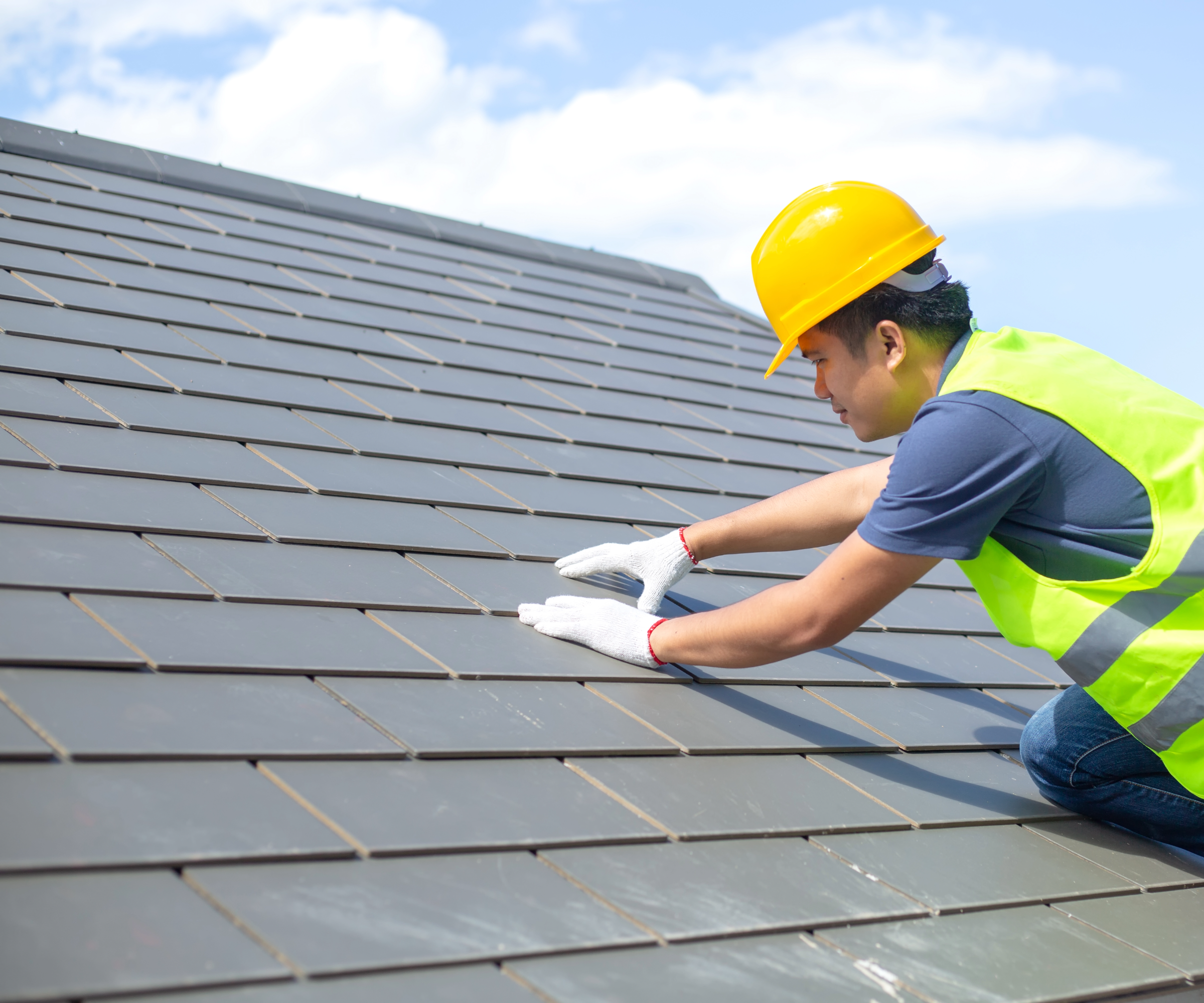 Person wearing high vis vest and helmet on a roof with their hands on tiles
