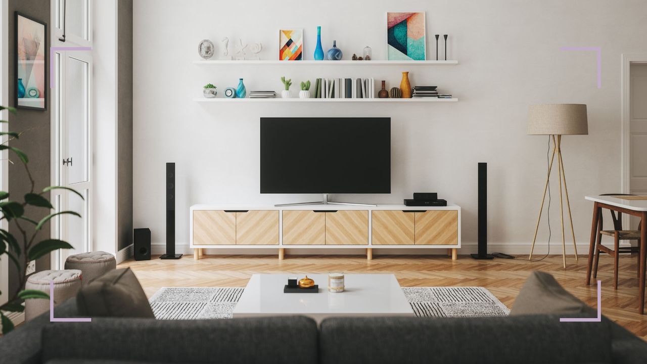 a clean living room with a TV on a wood stand, floating shelves, and a dark grey sofa in the foreground, with purple corners around it, to illustrate how to clean your house