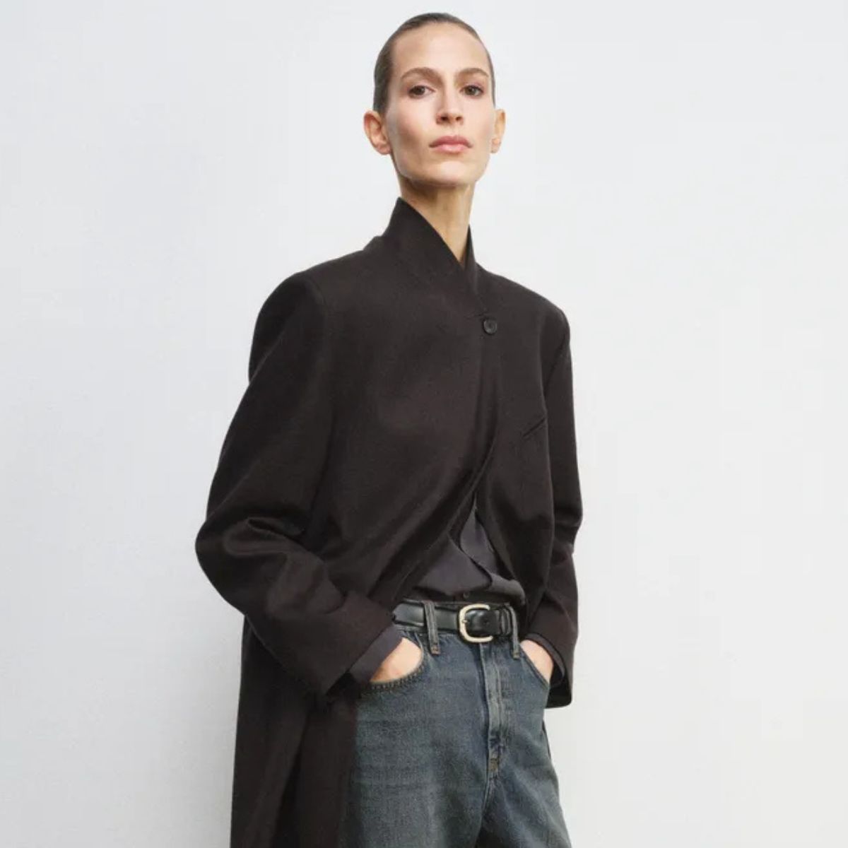 Model wears black high neck coat, blue jeans