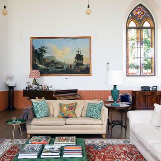 living room with white sofas and green ottoman and oriental rug with arched stained glass window behind