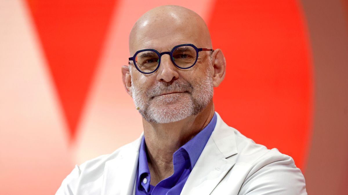  Bestselling Novelist, writer, Executive Producer, Harlan Coben against a red background wearing a light suit and blue glasses